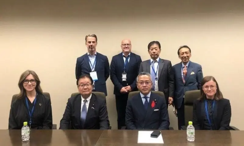 A group of eight people in business attire posing for a formal meeting photo around a conference table.